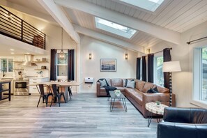 A spacious living area with a high ceiling, a dining table, a sofa, and a view of the outdoors.