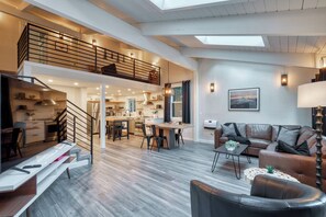 En rummelig loftlejlighed med mezzanin, køkken, spiseområde og opholdsstue med sofa og sofabord.