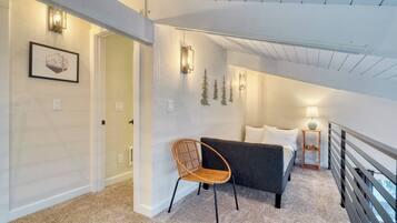 A bedroom with a bed, a chair, a nightstand, and a lamp. There is a door leading to another room.