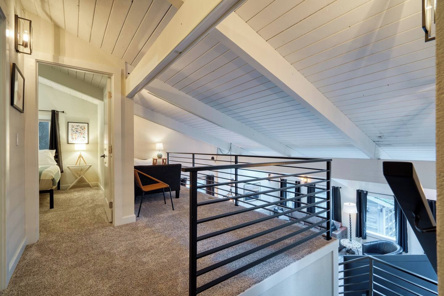 A spacious loft bedroom with a high ceiling, a staircase, and a view of the outdoors.