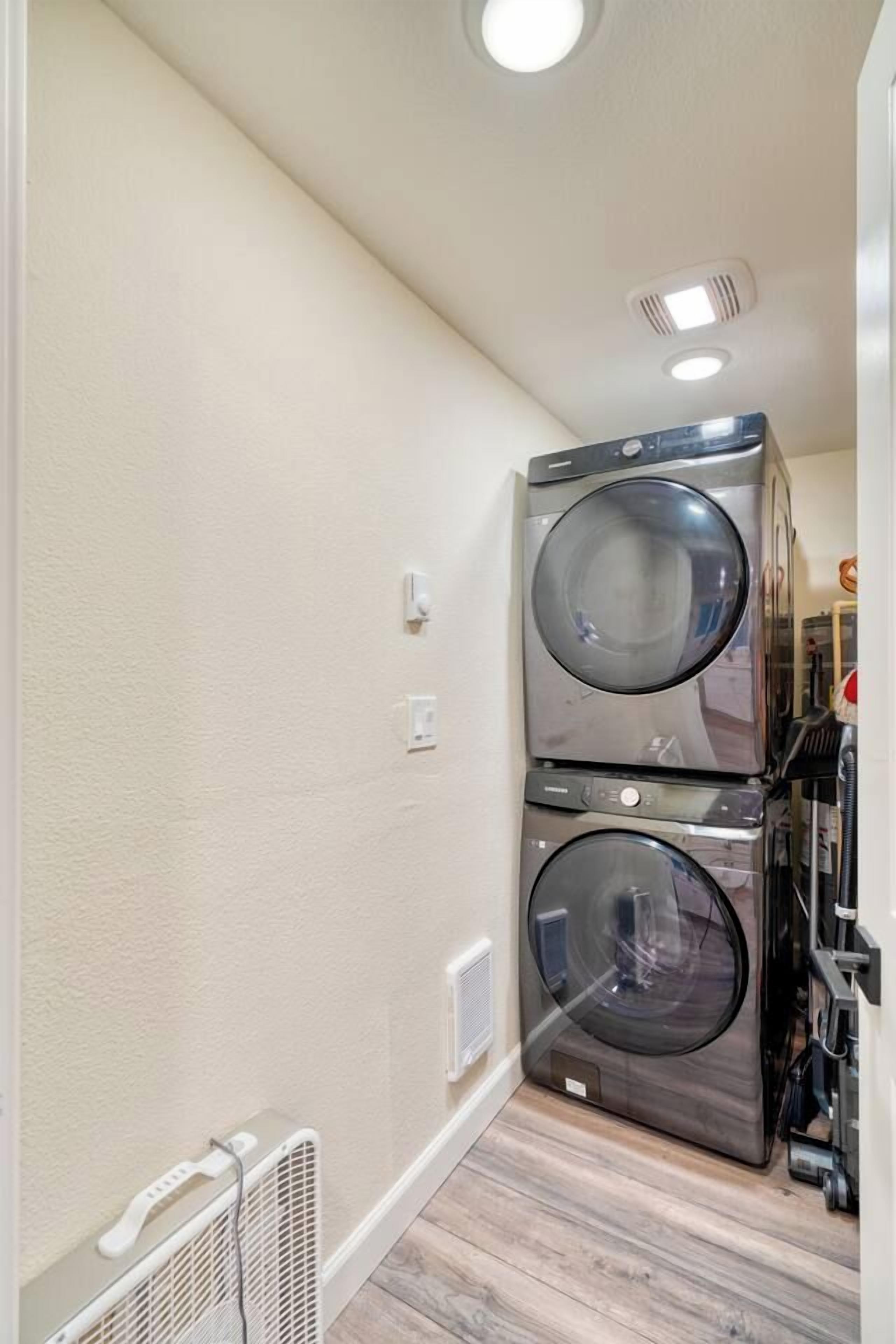 A laundry room with two stacked front-loading washers and dryers, a white radiator, and a ceiling vent.