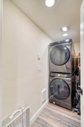 Et vaskerum med to stablede vaskemaskiner og tørretumblere, en hvid radiator og en ventilation i loftet.