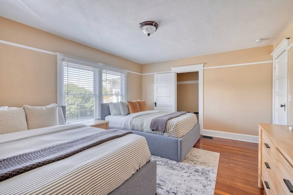 A bedroom with two beds, a wardrobe, and a window with blinds. - Your Front Door Opens onto Mississippi Ave (Portland)