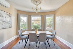 Une salle à manger avec une table, des chaises, un lustre et de grandes fenêtres.