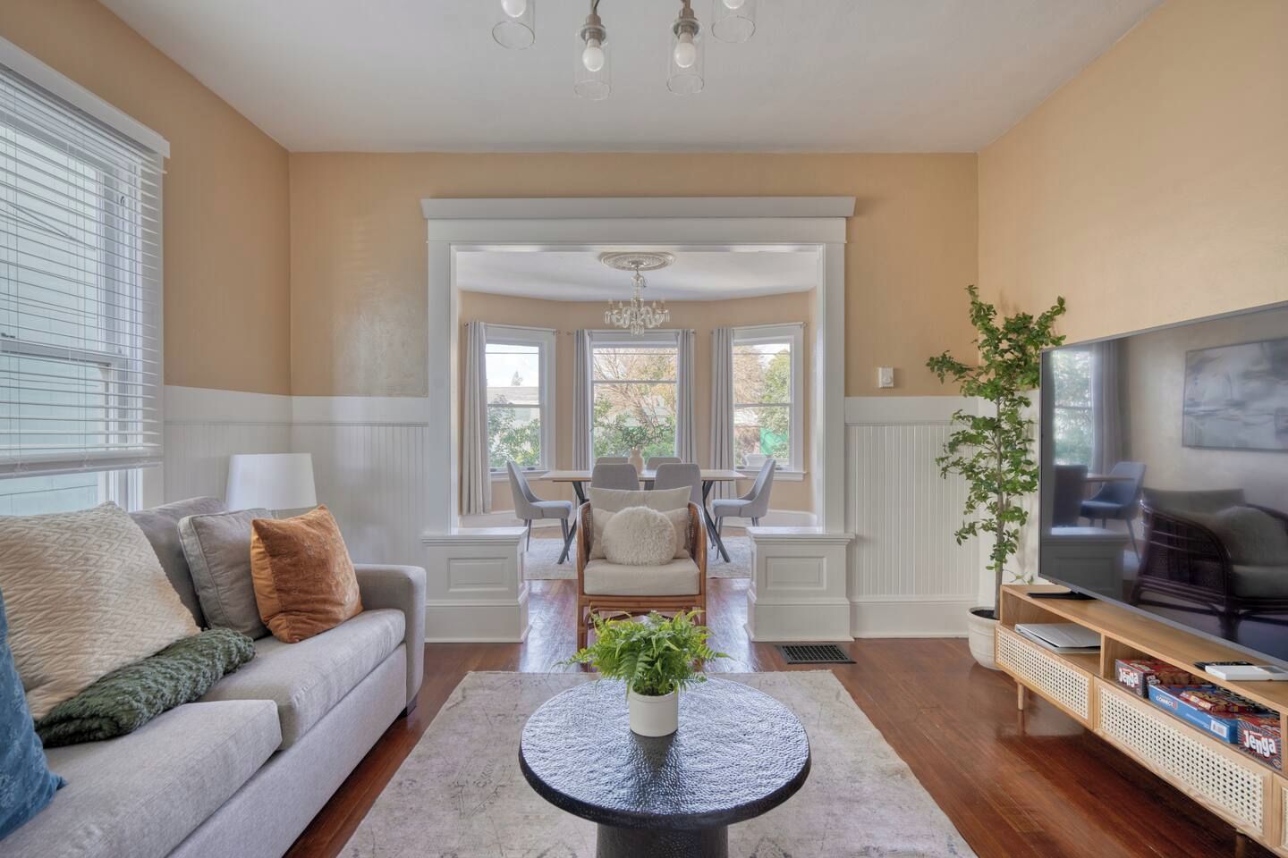 A living room with a sofa, a coffee table, a television, and a dining area in the background.