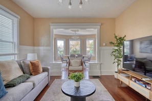 A living room with a sofa, a coffee table, a television, and a dining area in the background. - Your Front Door Opens onto Mississippi Ave (Portland)