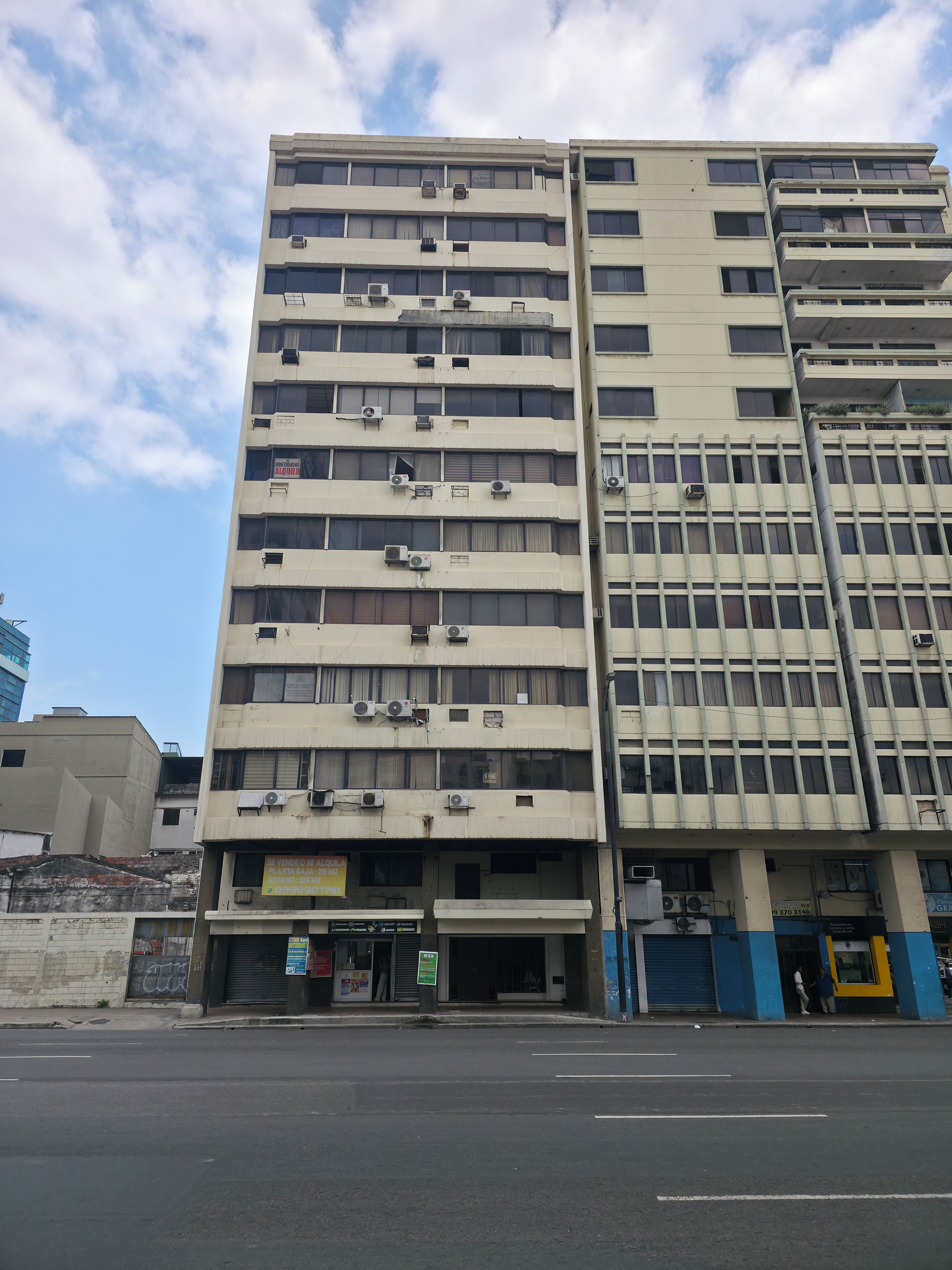 Un edificio de varios pisos con múltiples unidades de aire acondicionado, entrada a nivel de calle y un escaparate visible.