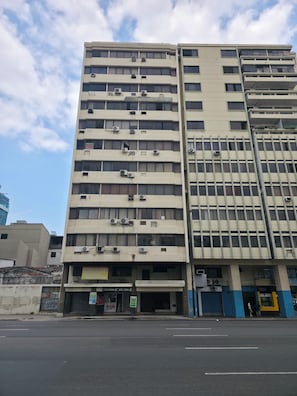 Un edificio de varios pisos con múltiples unidades de aire acondicionado, entrada a nivel de calle y un escaparate visible.