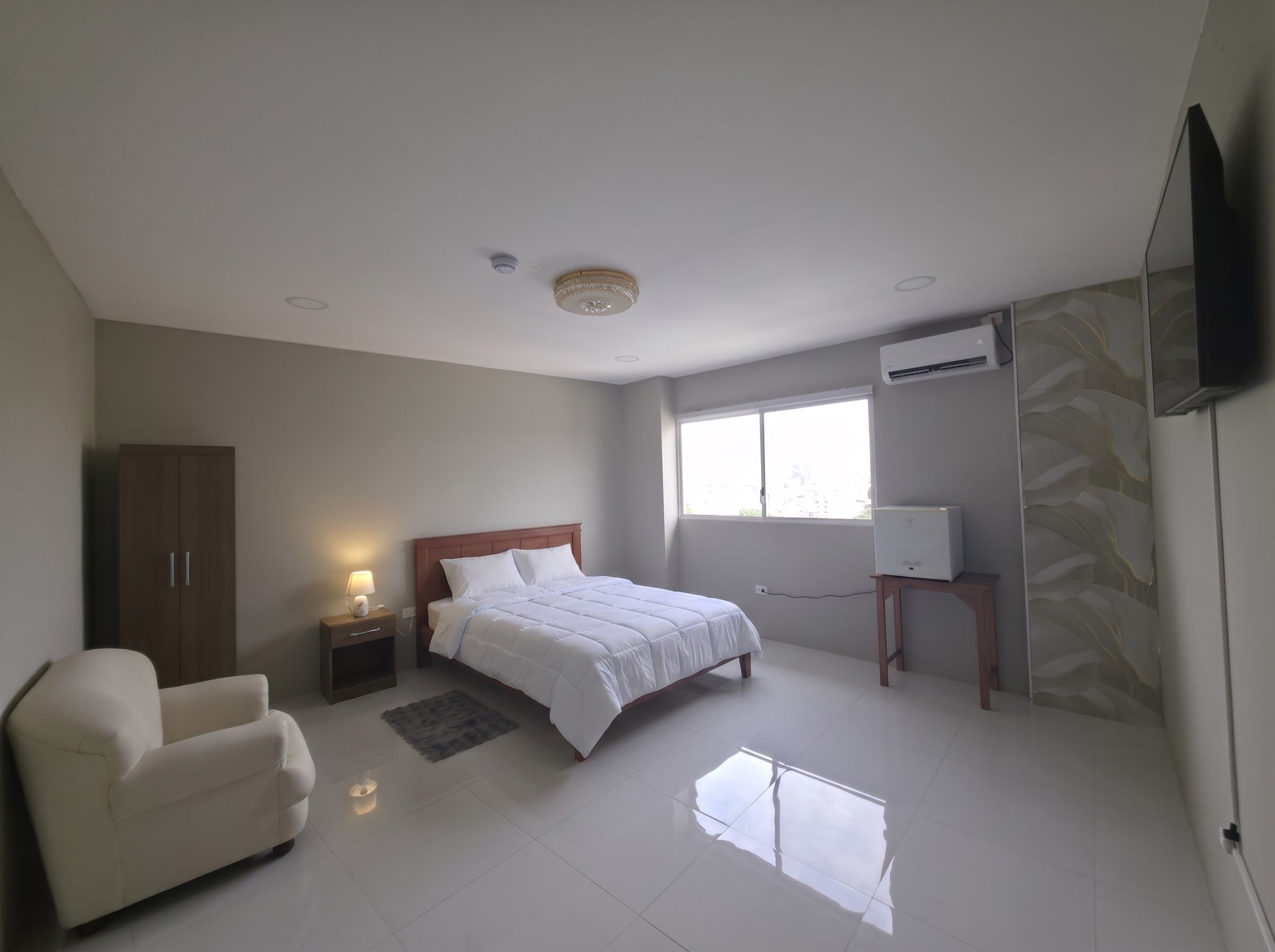 Habitación de hotel con cama, mesita de noche, lámpara, armario, silla y televisor en la pared.