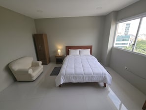Un dormitorio con cama, una silla, un armario, una mesita de noche y una ventana.