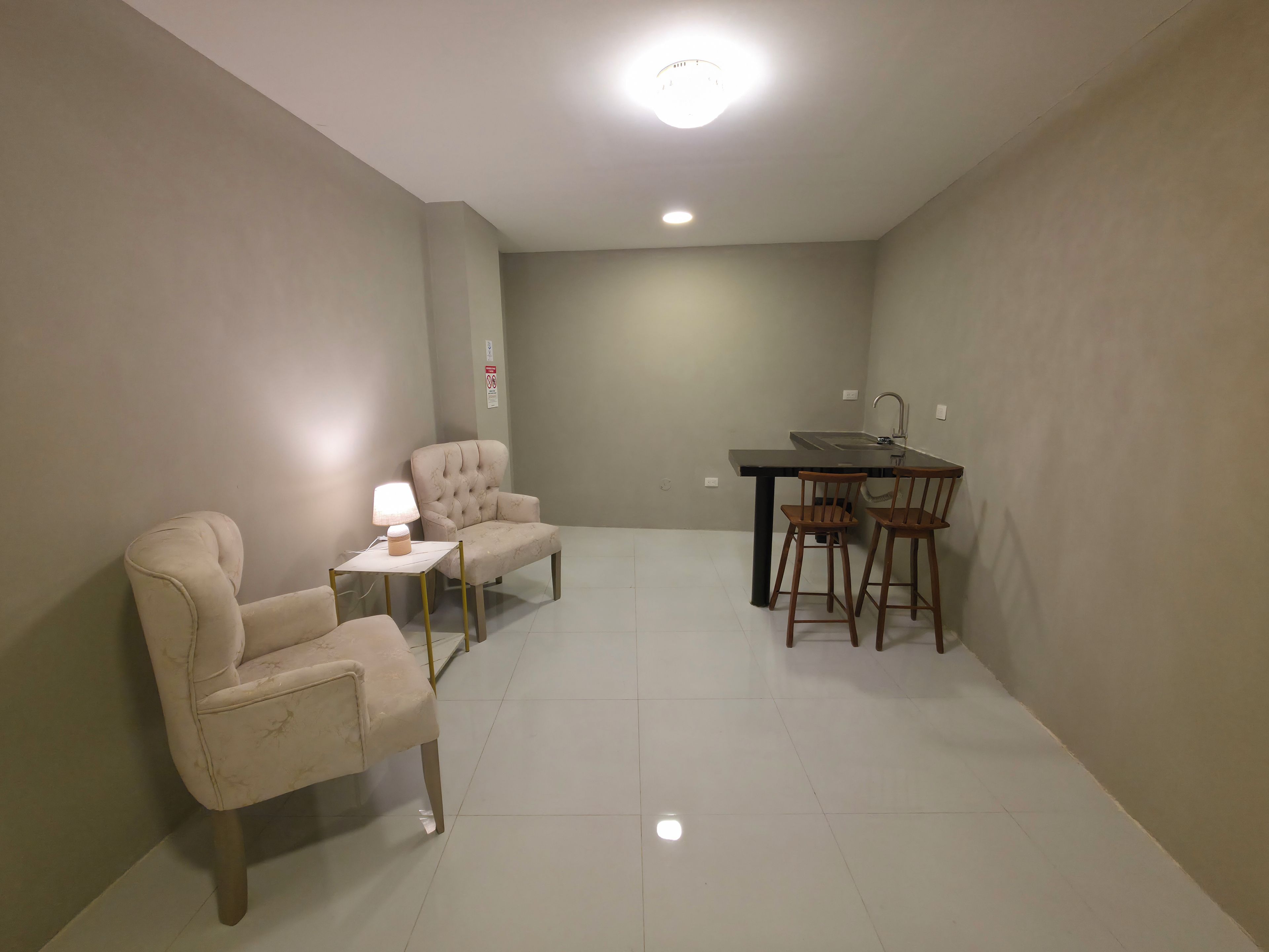 Una habitación pequeña y bien iluminada con una mesa de comedor, dos sillas, una lámpara y un sofá.