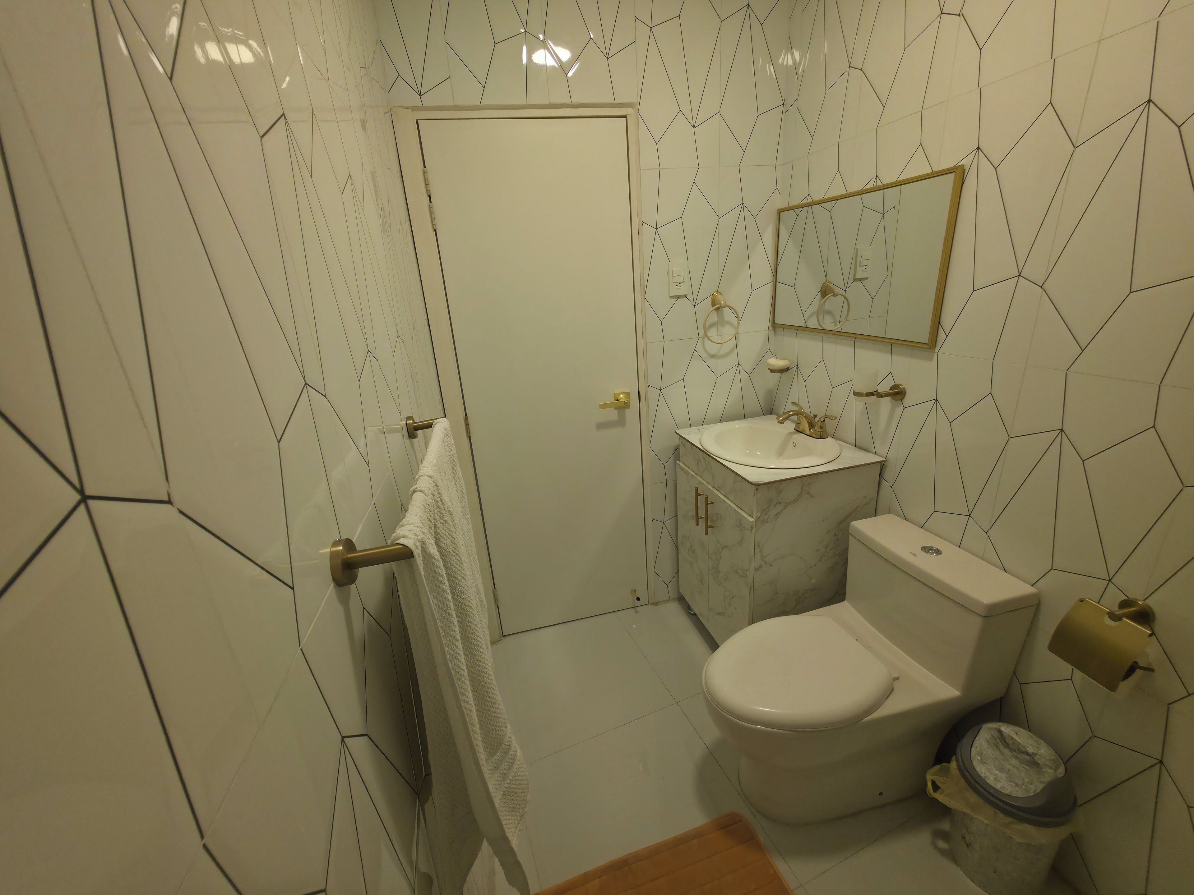 Un baño con inodoro blanco, lavabo con encimera de mármol y espejo sobre el lavabo.