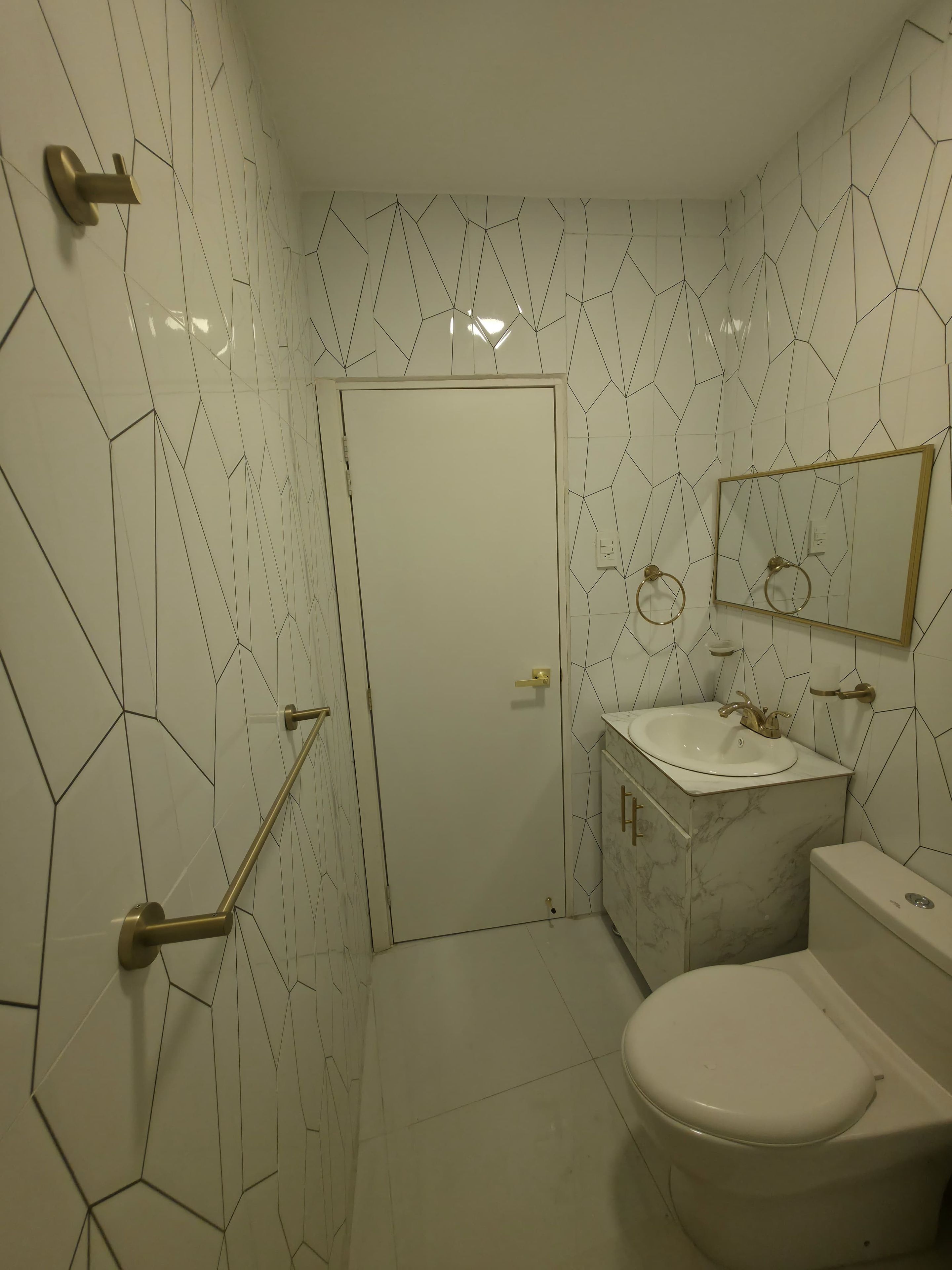 A bathroom with white hexagonal tiles, a white toilet, a marble sink, and a gold-framed mirror.