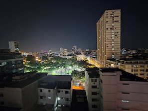 Un paisaje urbano nocturno con rascacielos, farolas y una avenida bordeada de árboles.