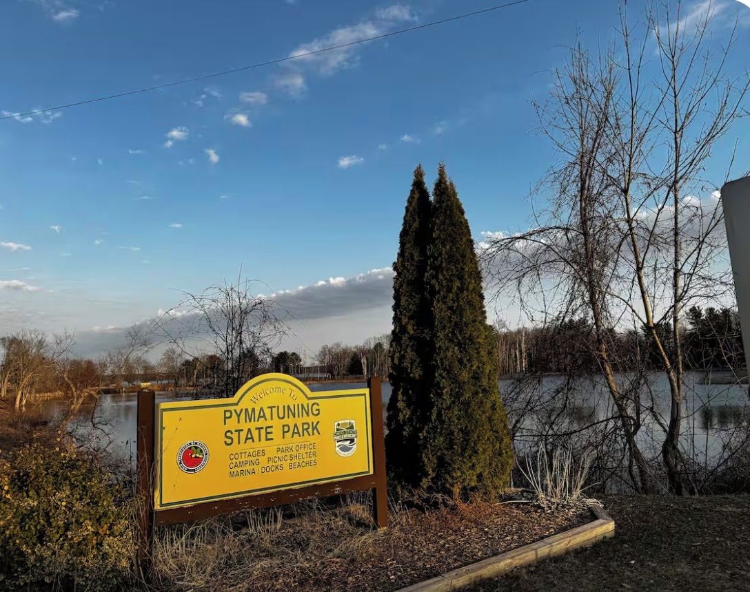 Welkomstbord voor Pymatuning State Park met vermelde faciliteiten zoals vakantiehuisjes, parkkantoor, picknickoverkapping, camping, jachthaven en steigers.