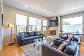 A modern living room with a sectional sofa, a glass coffee table, and a fireplace. - Alberta Arts 4BR • 5 Queen Beds • Sleeps 11 (Portland)