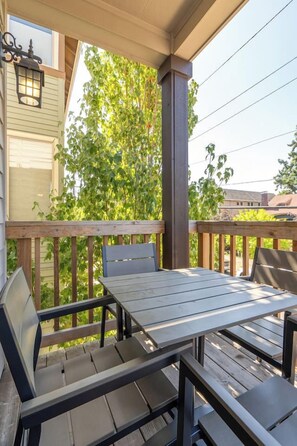 A wooden deck with a table and chairs, surrounded by greenery. - Alberta Arts 4BR • 5 Queen Beds • Sleeps 11 (Portland)