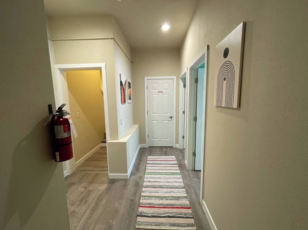 A hallway with a fire extinguisher, a bench, a door, and a wall-mounted artwork.