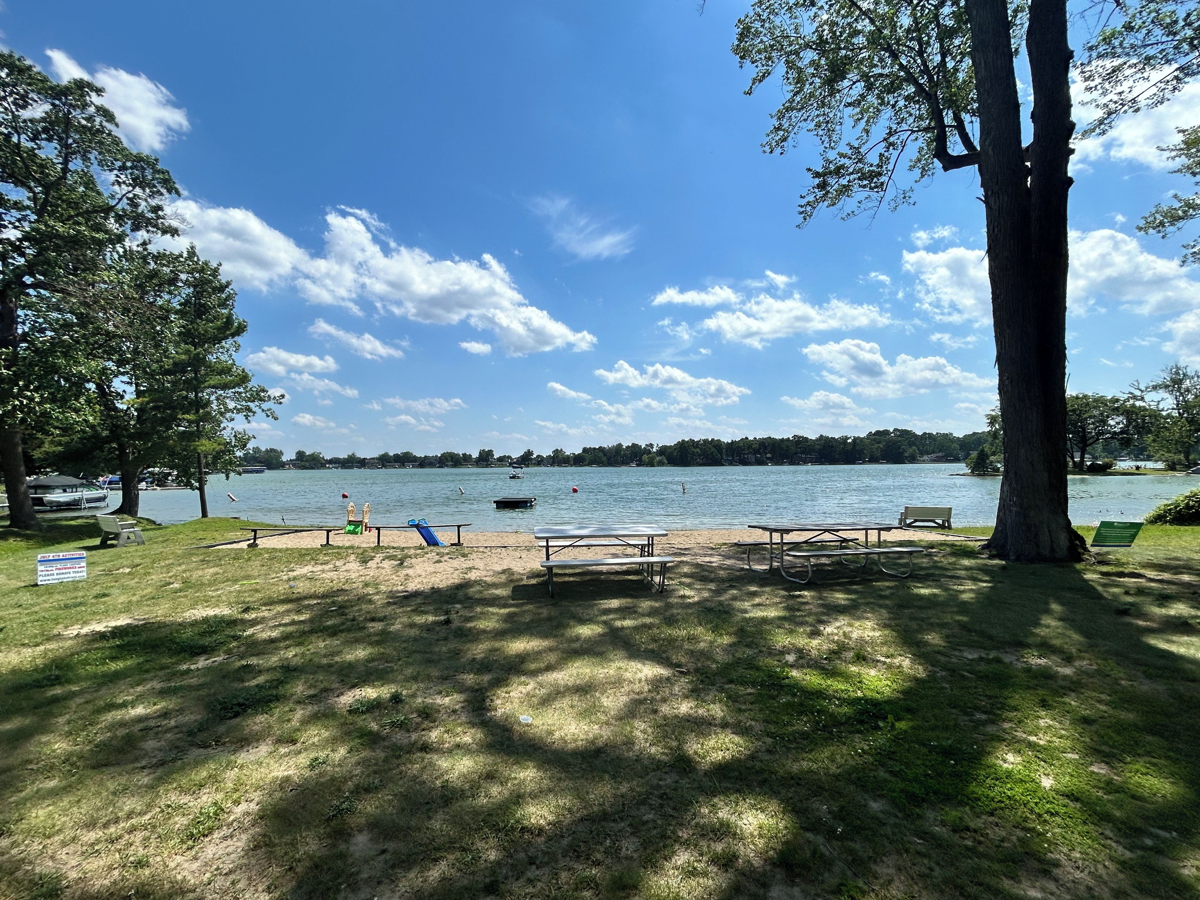A lakeside park with picnic tables, a playground, and a boat on the water.