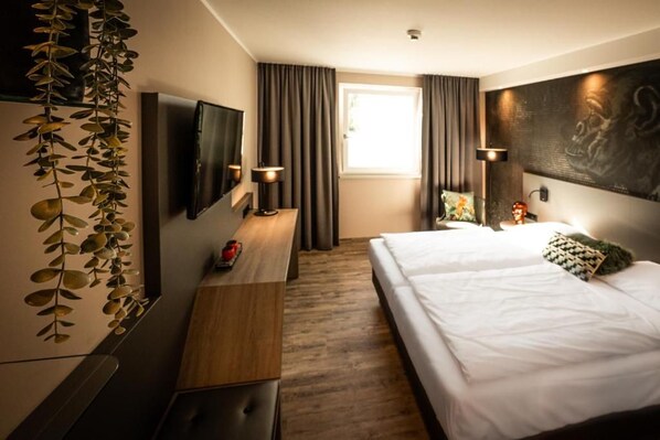 Ein Hotelzimmer mit Bett, Schreibtisch, Fernseher und einem Fenster mit Vorhängen.