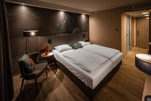 Ein modernes Hotelzimmer mit einem großen Bett, einem Sessel, einem kleinen Tisch und einem Wandbild.