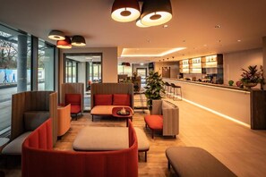 Eine moderne Hotelhalle mit Sitzbereichen, einer Bar und Blick ins Freie.