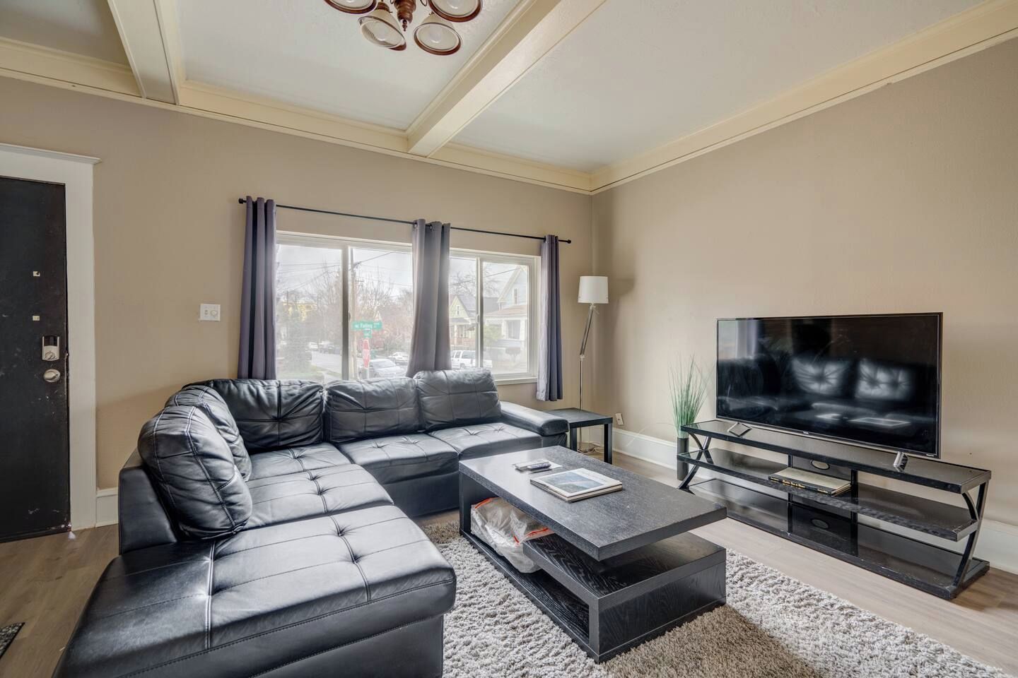 A modern living room with a sectional sofa, a flat-screen TV, and a glass coffee table.