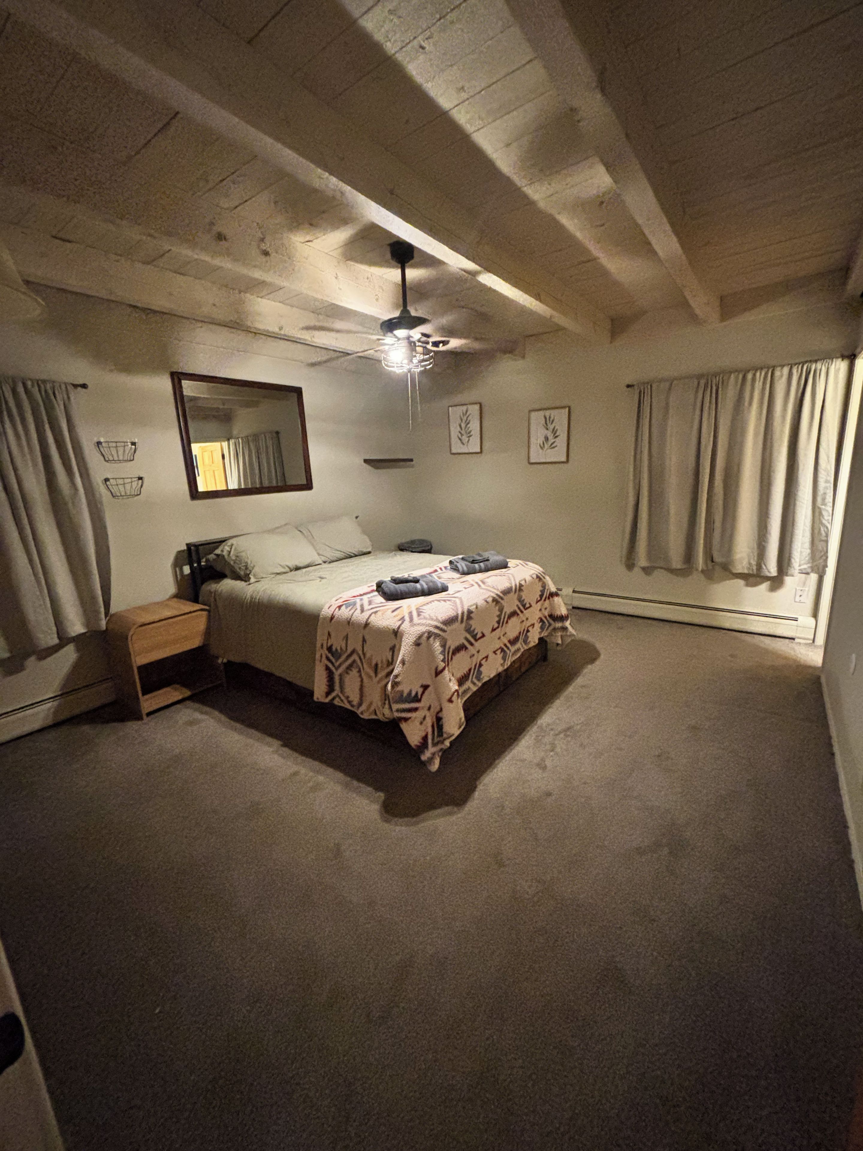 Een slaapkamer met een bed, nachtkastje, plafondventilator en een raam met gordijnen.