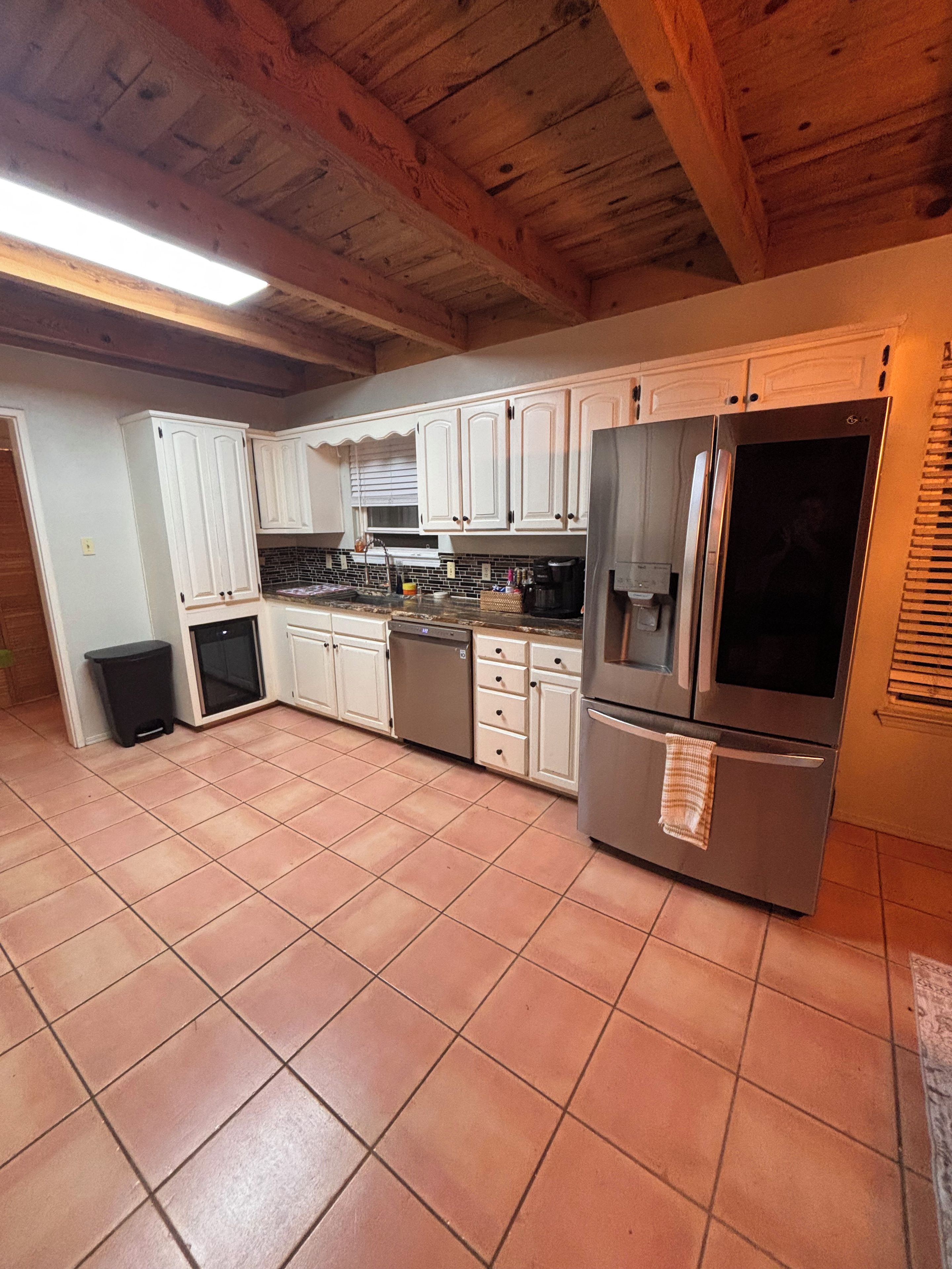 Una cocina con armarios blancos, un refrigerador de acero inoxidable y piso de baldosas.