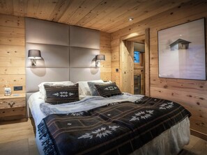 Una habitación acogedora de madera con una cama, dos lámparas de pared y un cuadro grande con marco.