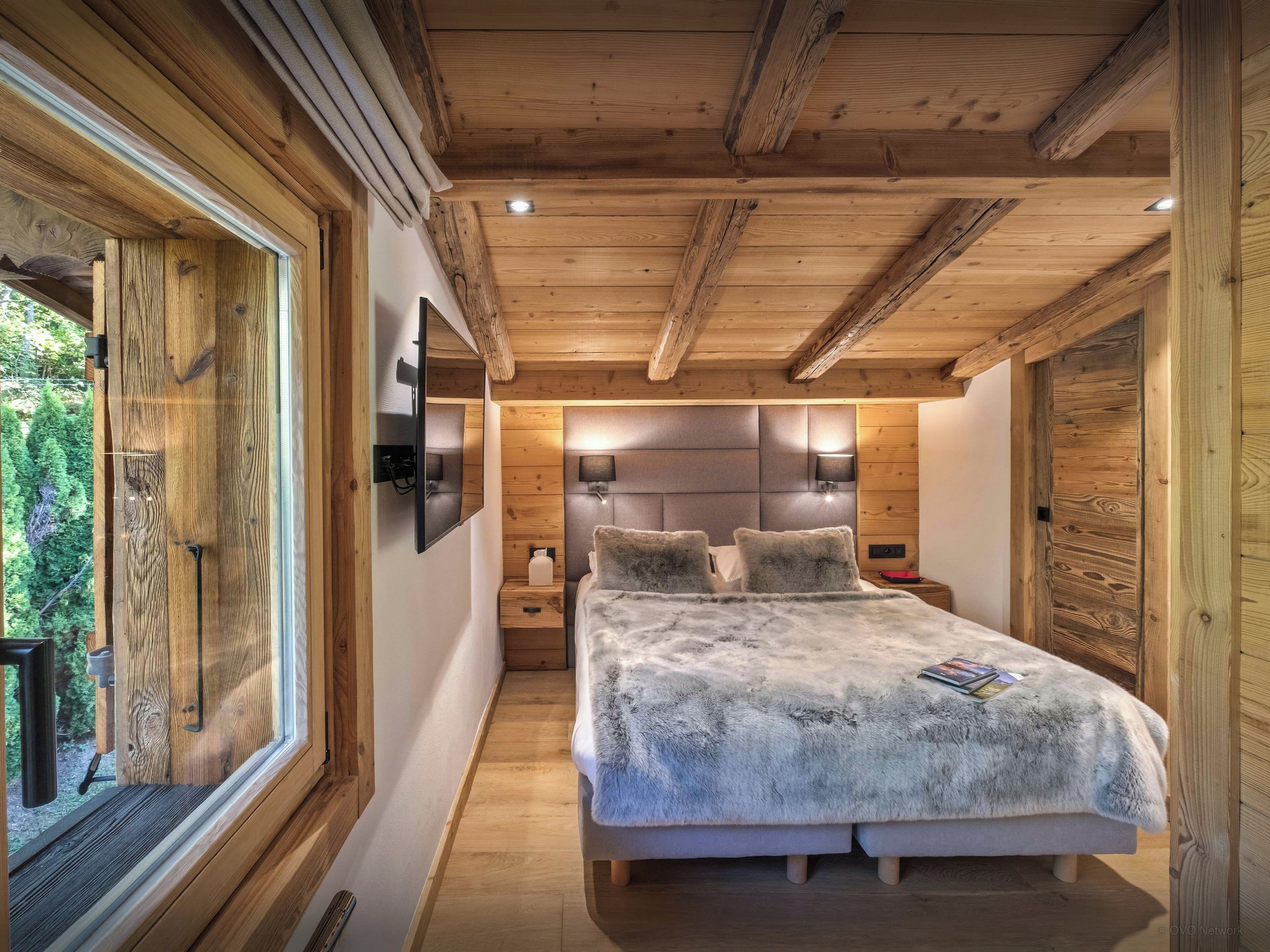 Une chambre avec un plafond en bois, un lit recouvert d’une couverture moelleuse, une table de chevet et un téléviseur fixé au mur.