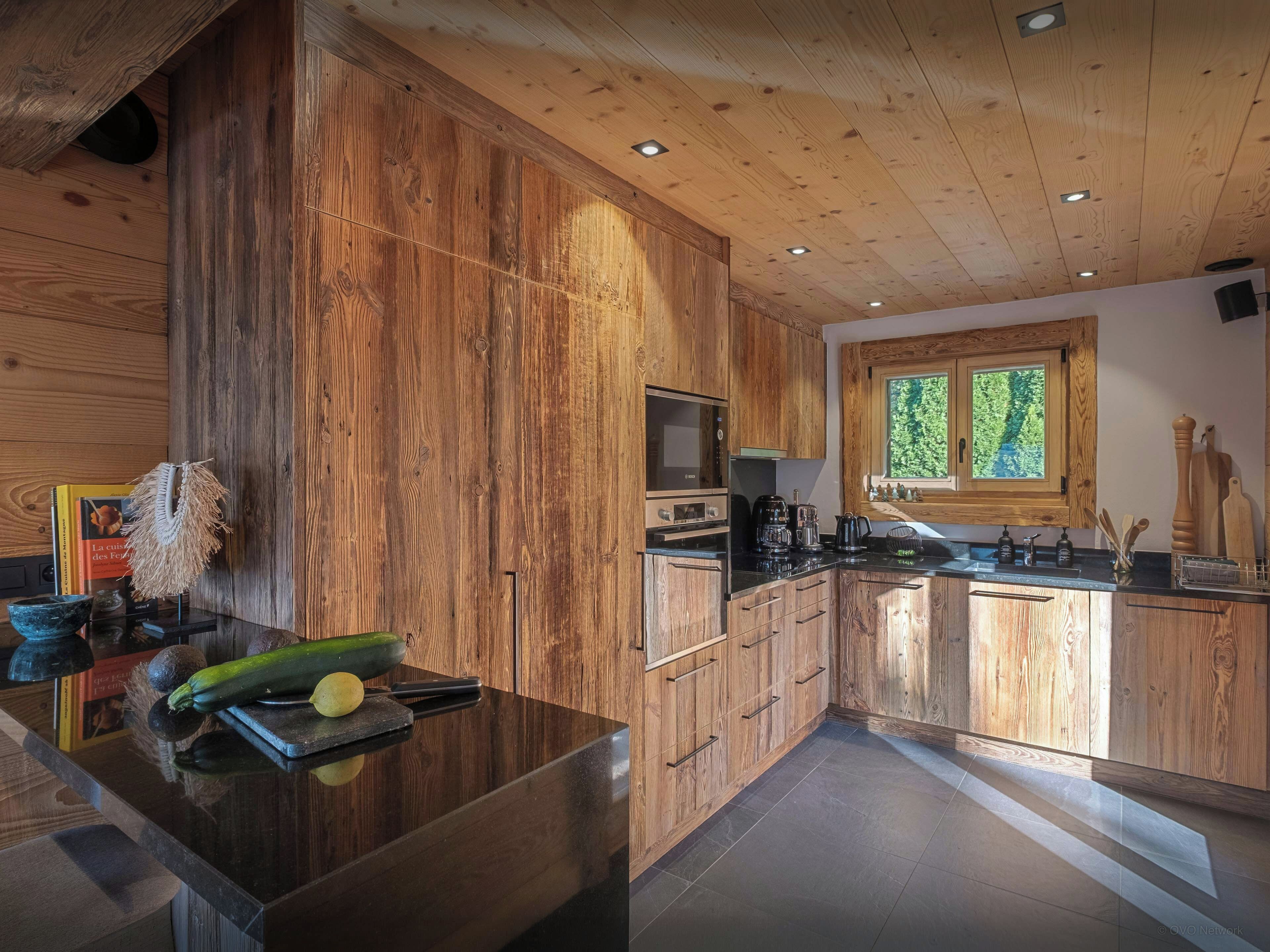 Une cuisine moderne avec des meubles en bois, un plan de travail noir et une fenêtre qui laisse entrer la lumière naturelle.