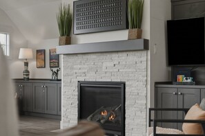 A modern living room with a fireplace, a mounted television, and decorative items. - Tetherow Luxe ~ Golf Views ~ Hot Tub ~ Pool Table (Bend)