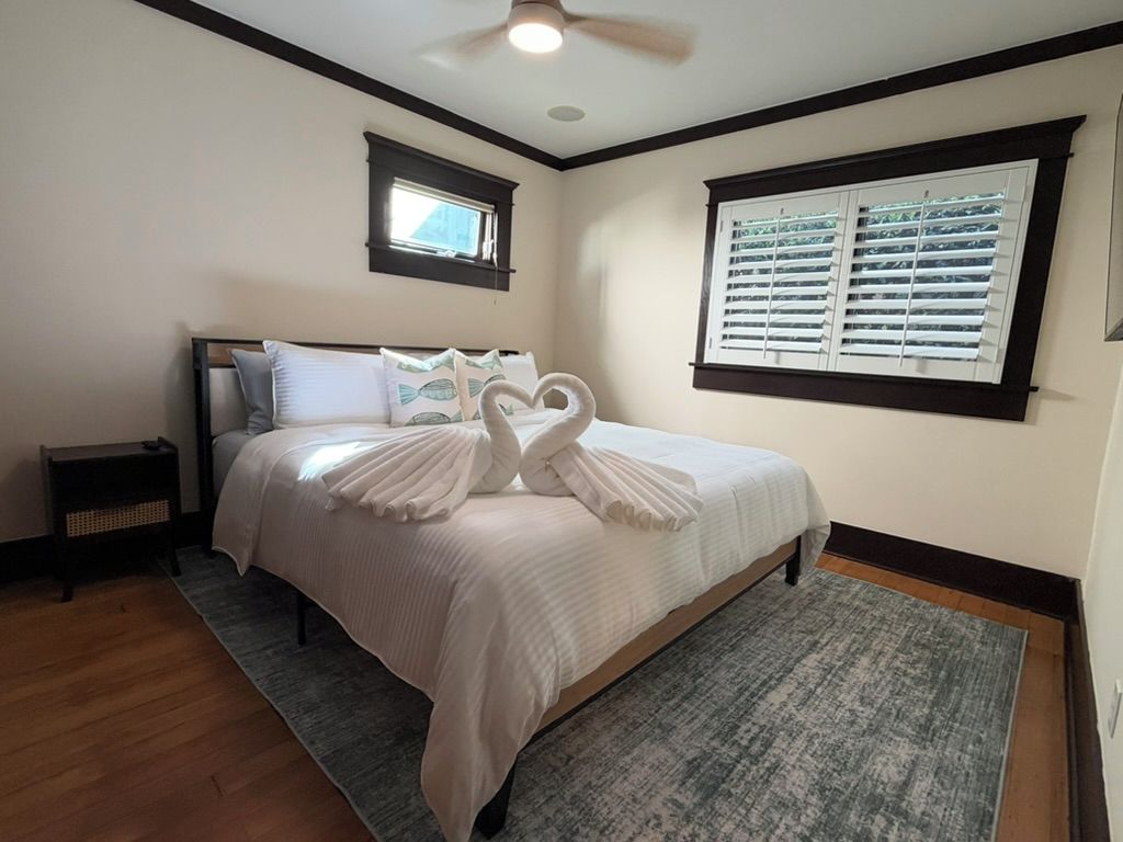 A bedroom with a bed, a nightstand, a window with blinds, and a ceiling fan.