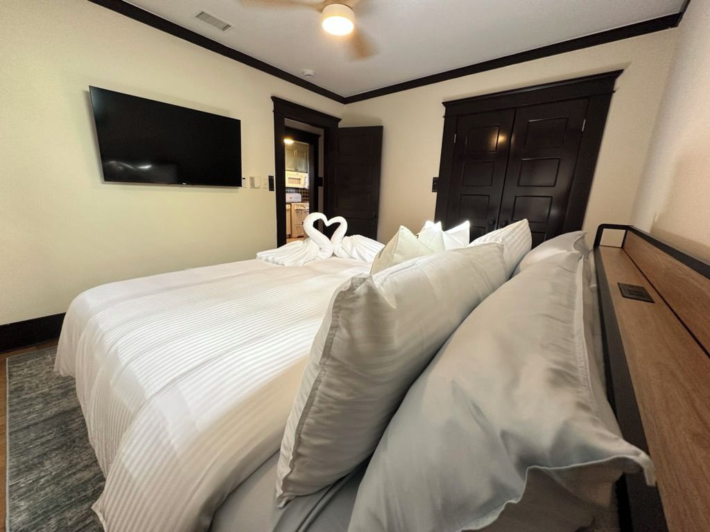 A hotel room with a bed, a flat-screen TV mounted on the wall, and a dark wooden door.