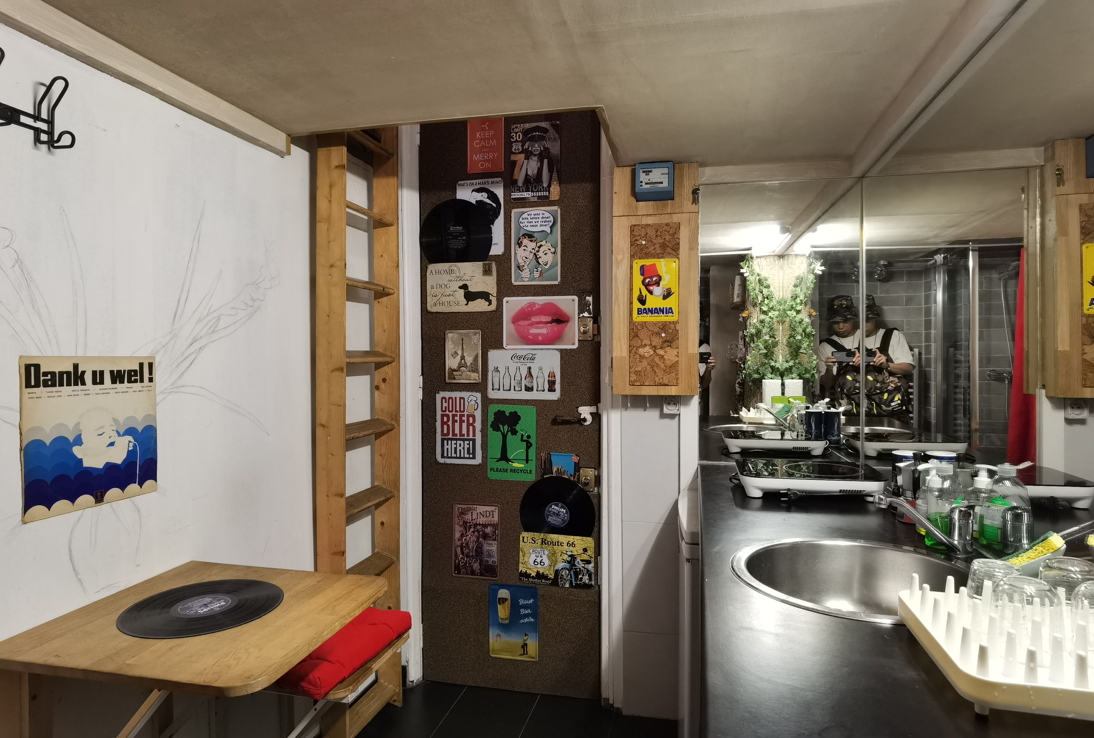 A compact kitchen with a sink, wooden counter, and various decorative items including a vinyl record, a Coca-Cola sign, and a 'Thank u well!' sign.