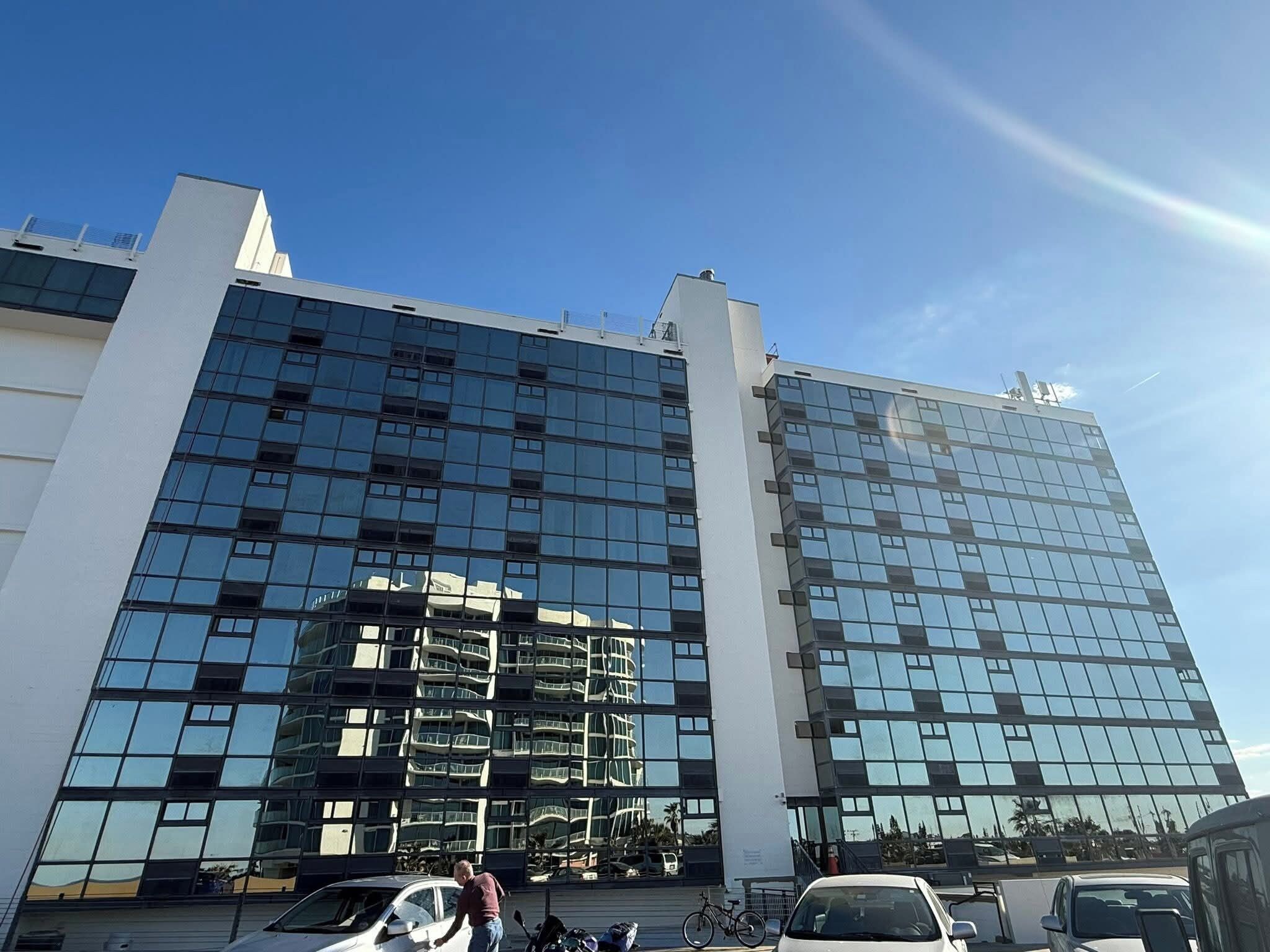 Un bâtiment moderne doté d’une façade en verre réfléchissant, de plusieurs étages et surplombant un ciel dégagé.
