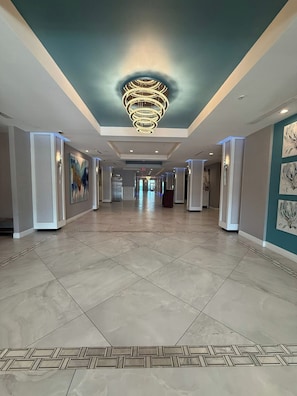 Een hotelgang met een moderne kroonluchter, betegelde vloer en kunstwerken aan de muren.