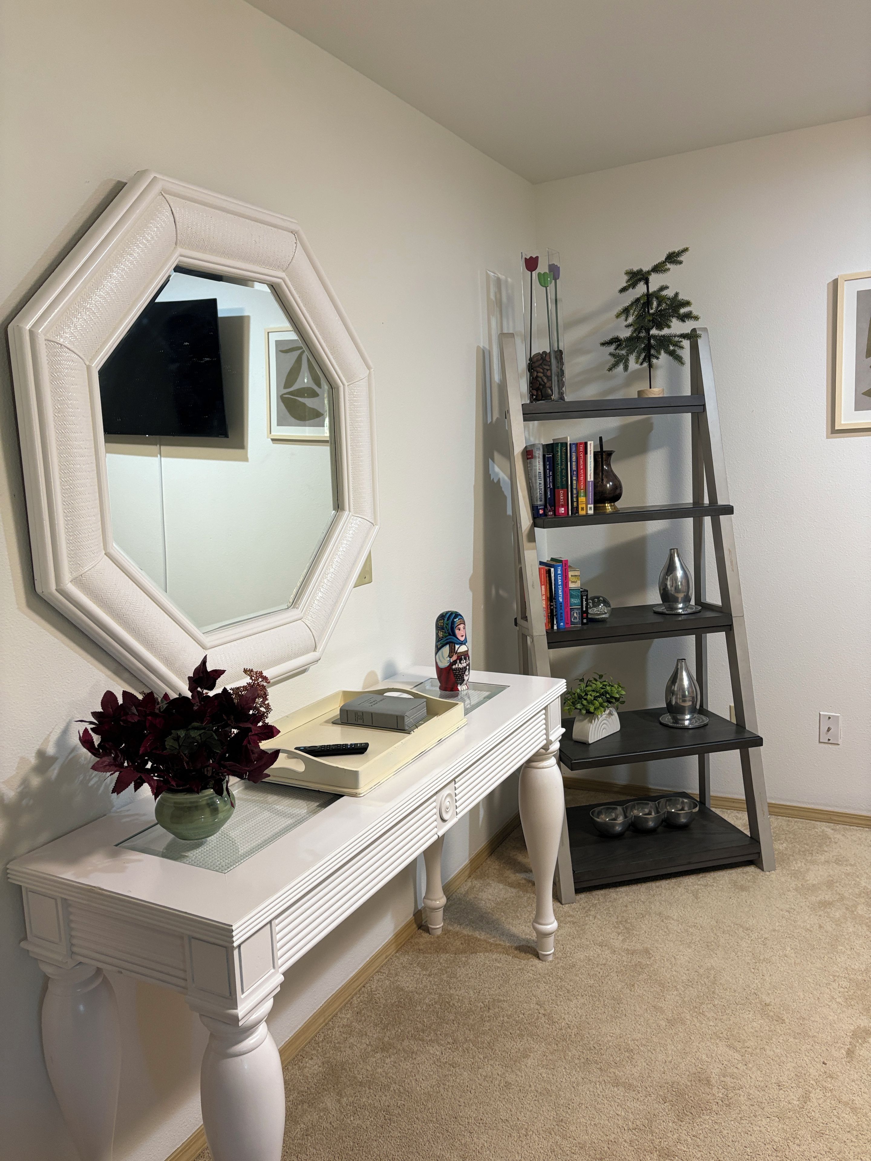 A room with a white console table, a large mirror, a bookshelf, and a ladder.