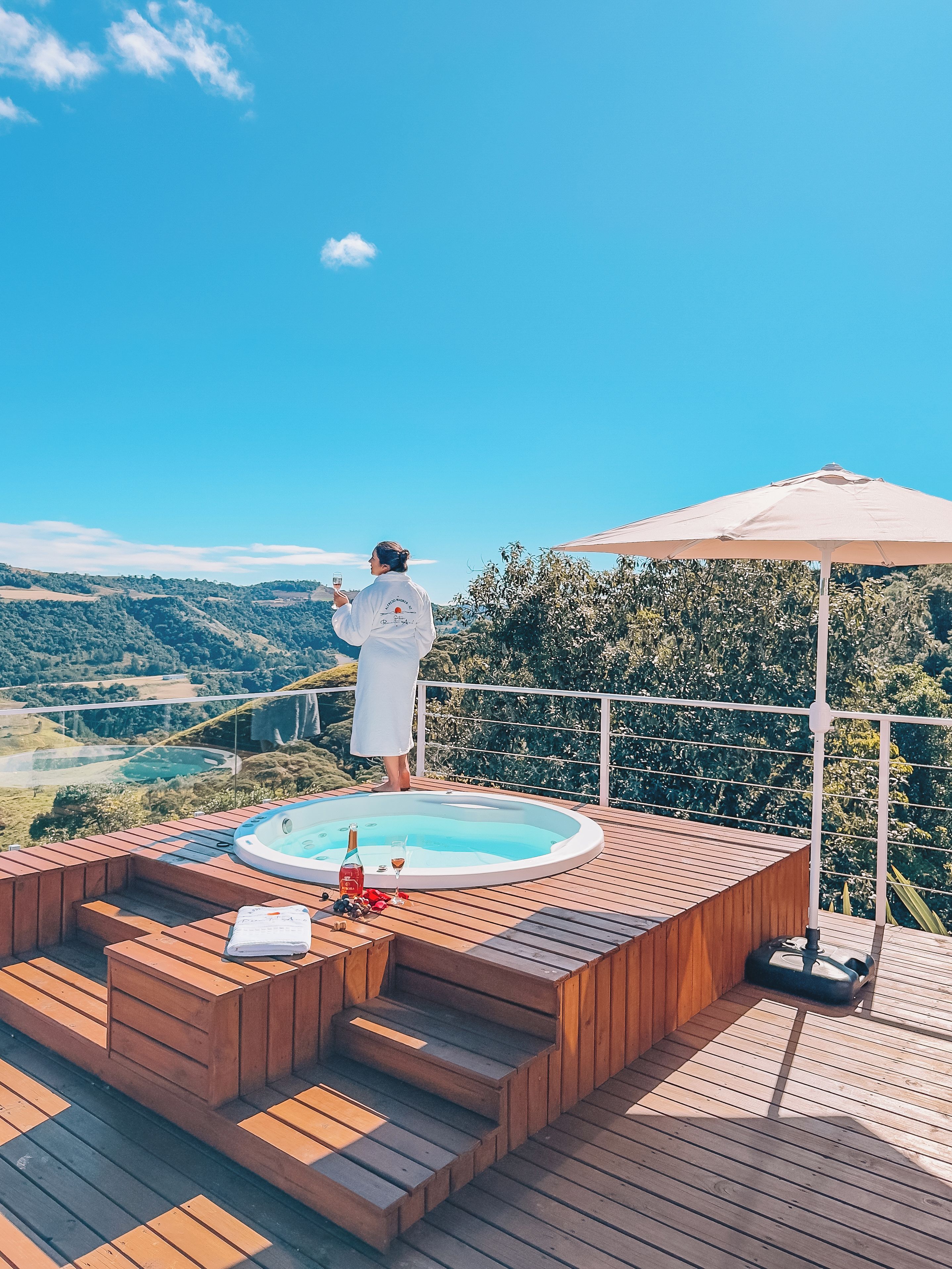 A person in a white robe standing by a hot tub with a scenic view.