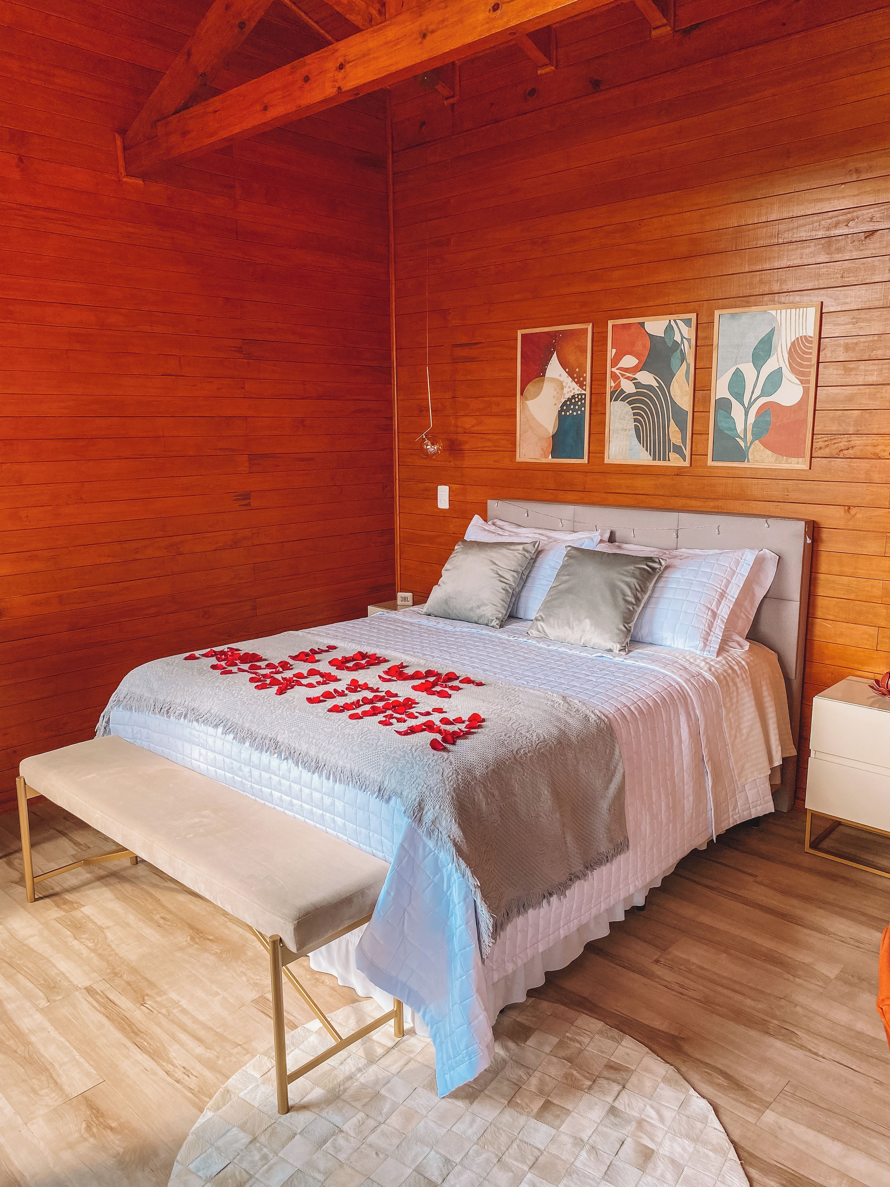 Ein Schlafzimmer mit Holzboden, einem Bett mit einer Steudecke, Kissen und einer Bank. Über dem Bett befinden sich zwei Wandbilder.