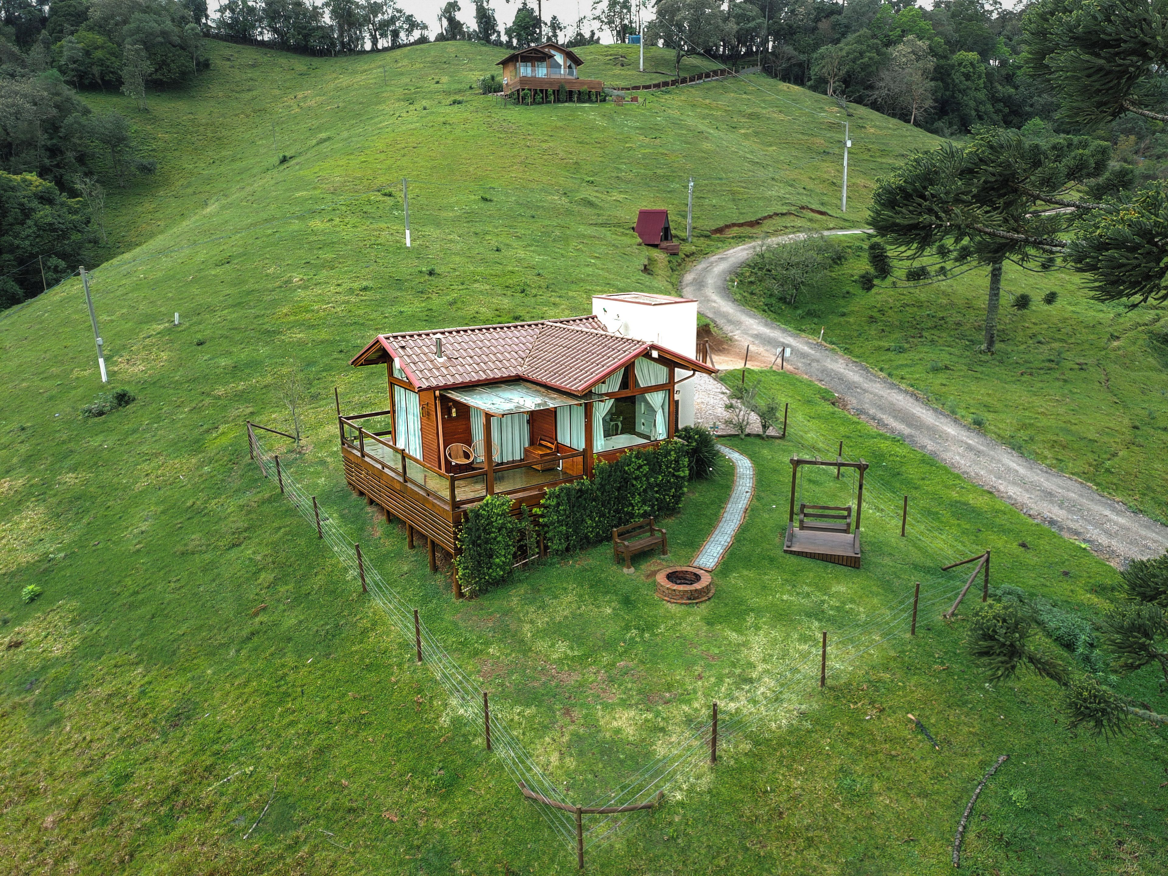 Una casa de madera con balcón, rodeada por un patio cercado y un camino de tierra.