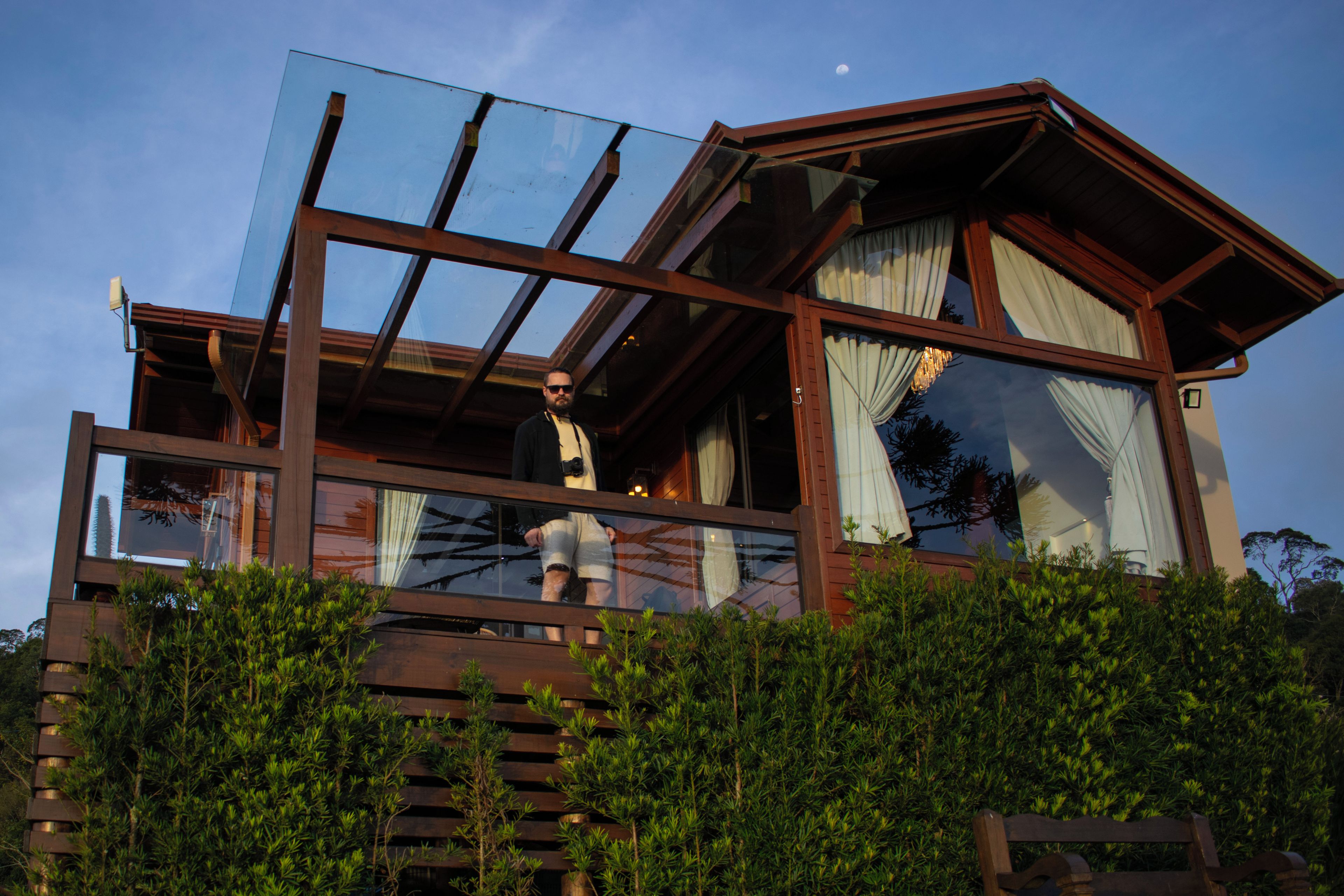 A wooden cabin with a glass balcony, a wooden deck, and a view of the sky.