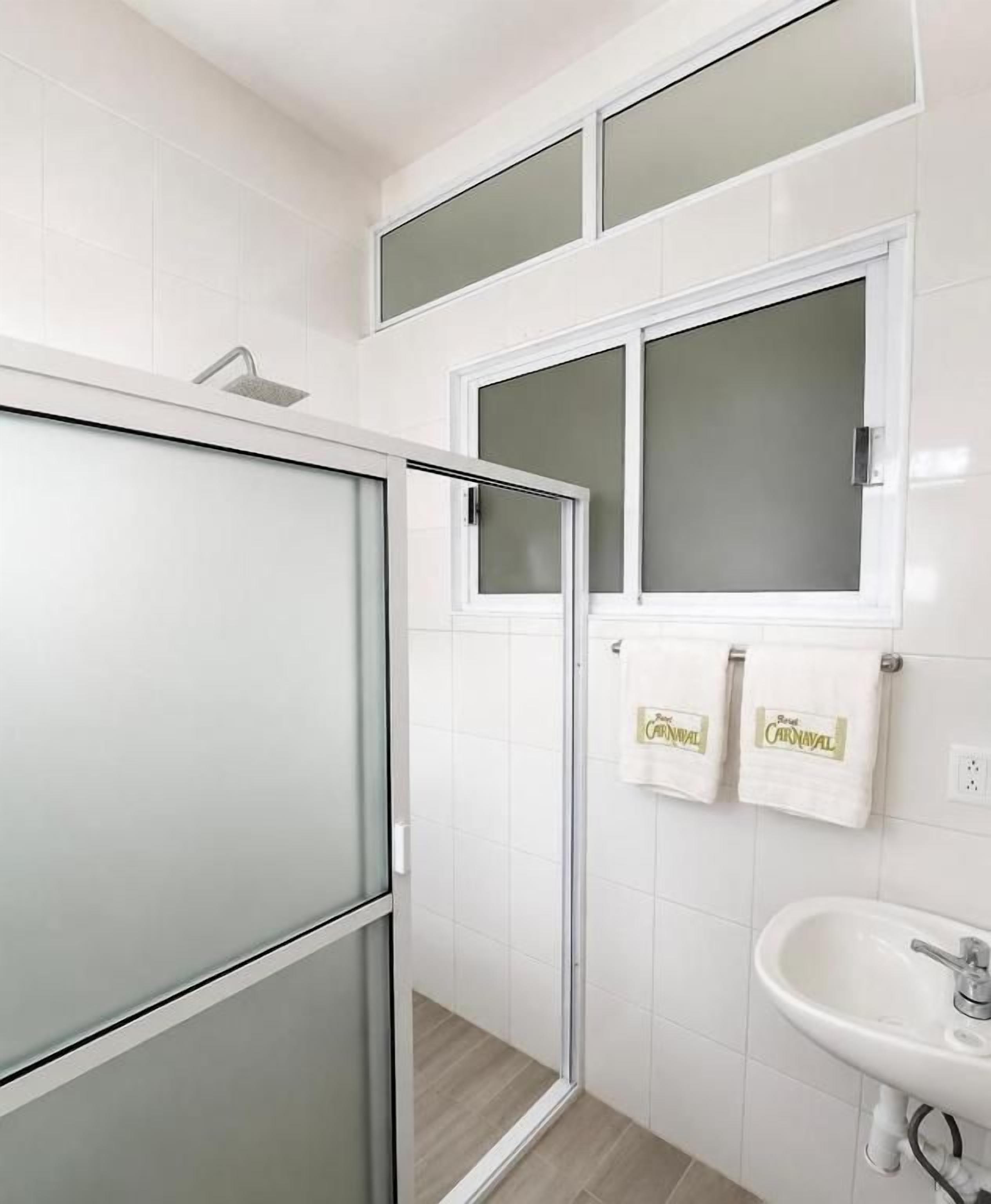 A bathroom with a glass shower enclosure, a sink, and two towels hanging on a rack.