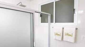 A bathroom with a glass shower enclosure, a sink, and two towels hanging on a rack.