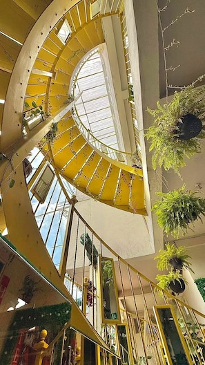 A spiral staircase with yellow railings inside a building, surrounded by greenery and glass railings.