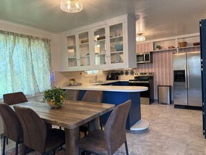 Ett modernt kök med en central köksö, vita köksskåp, vitvaror i rostfritt stål och en matplats med ett träbord och stolar.