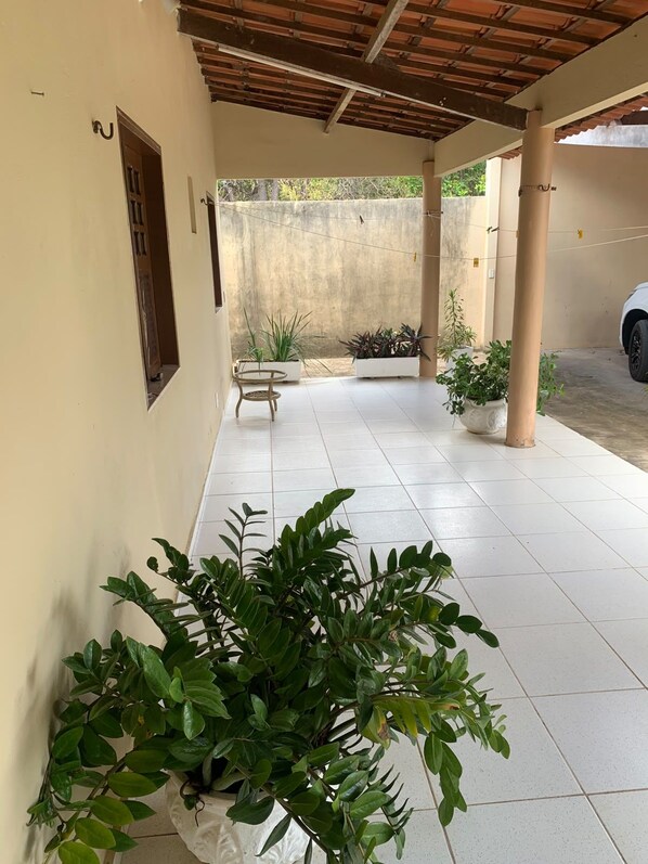 A covered outdoor area with tiled flooring, potted plants, and a bench.