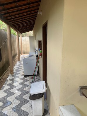 A corridor with a tiled floor, a washing machine, a trash bin, and a broom leaning against the wall.