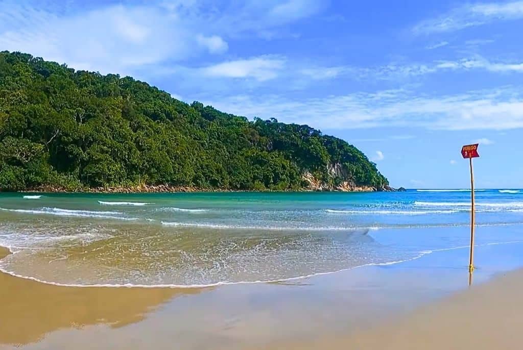 Una playa con agua turquesa cristalina, una orilla arenosa y una colina boscosa al fondo.
